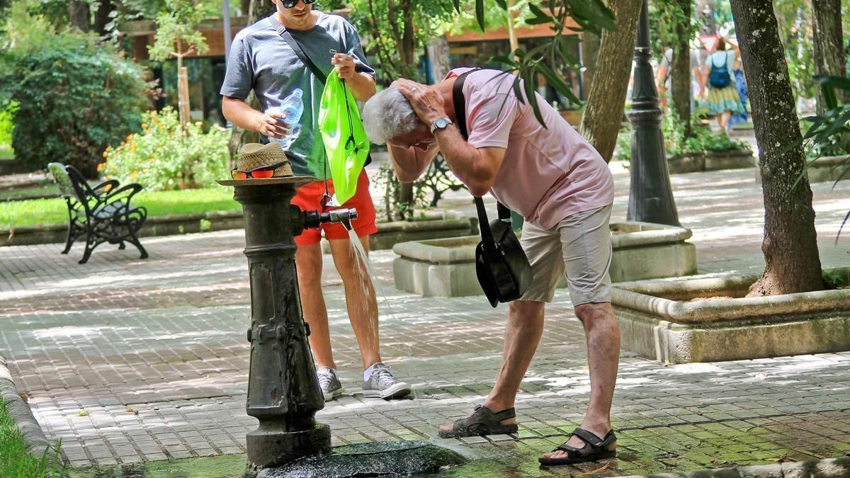 Dos cacereños se alivian el calor en una fuente.