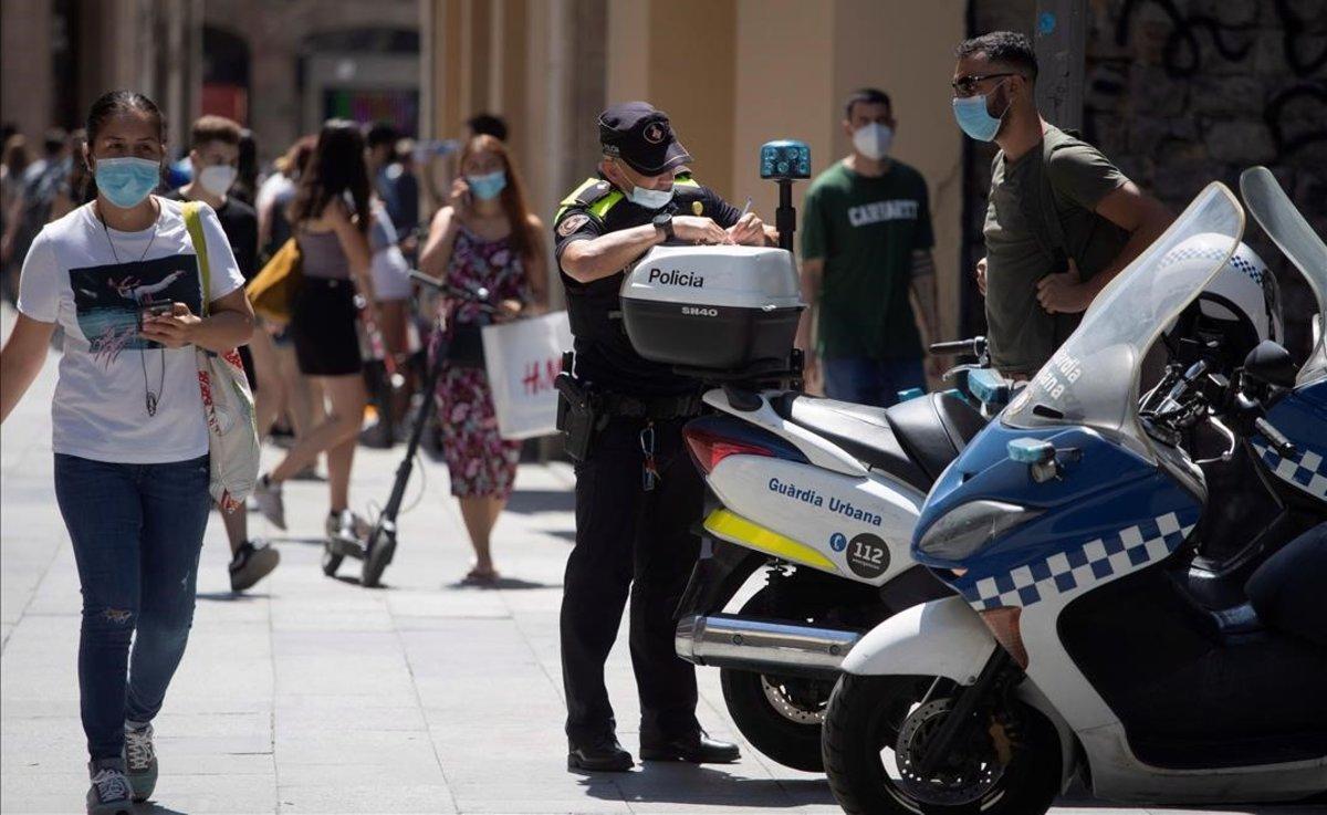 Un policía multa a un ciclista por una infracción y le advierte también de que debe usar mascarilla cuando vaya por la calle, en Barcelona, el pasado 11 de julio.