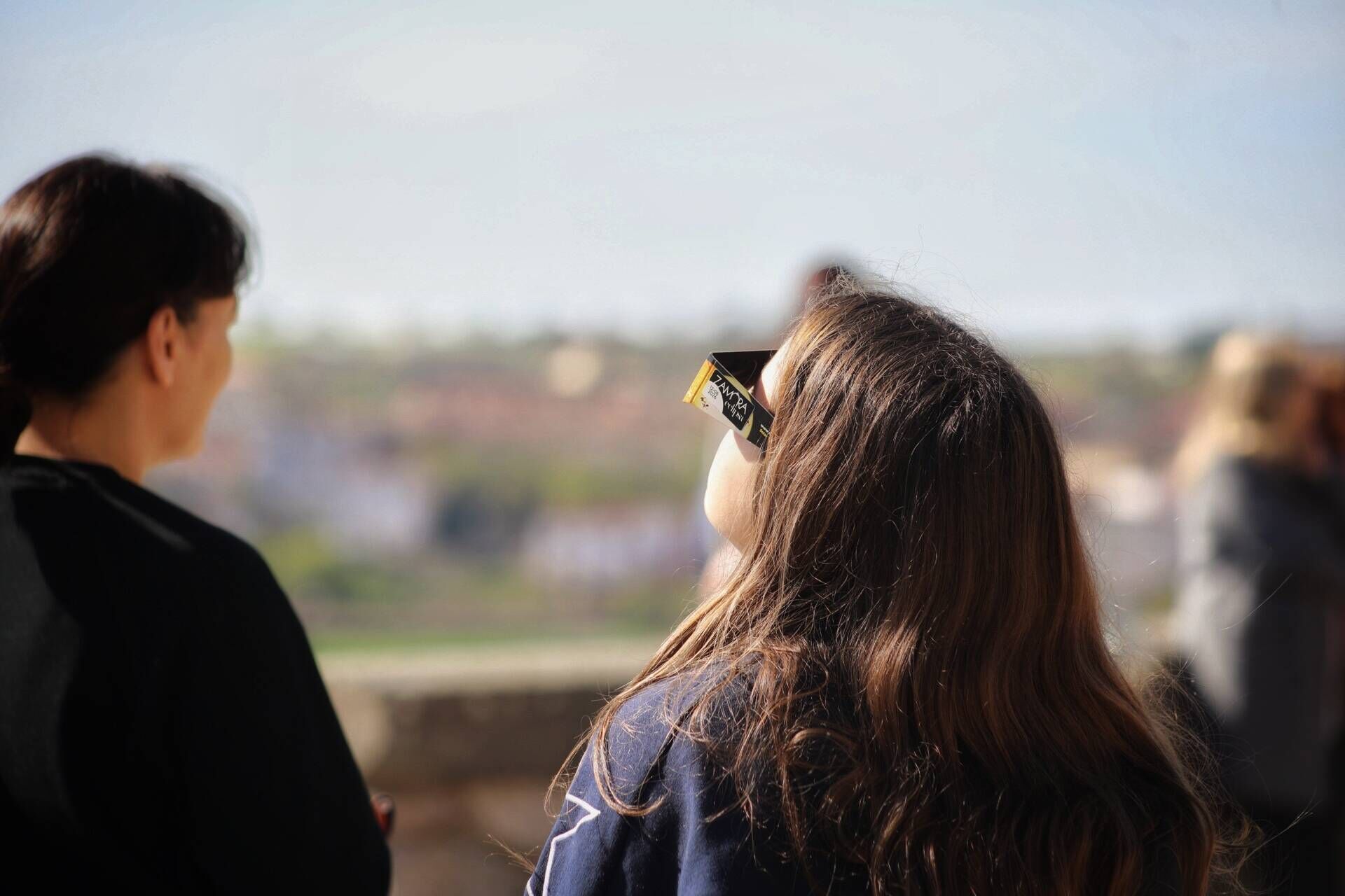 Una mujer mira al cielo con unas gafas destinadas a la observación del eclipse solar.