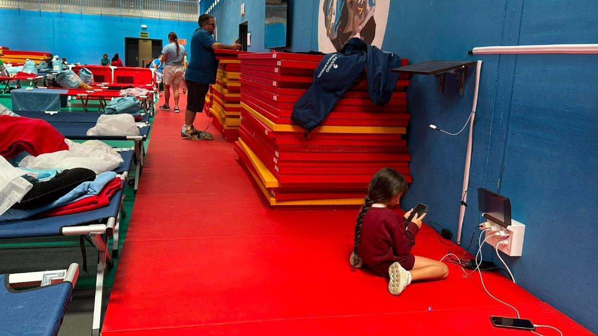 Una niña, en el punto de acogida de Villaviciosa de Odón, carga el móvil mientras las familias evacuadas esperan noticias sobre sus casas.