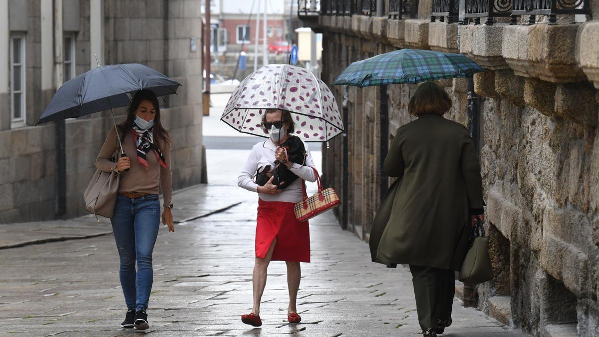 Varias personas con paraguas y prendas de abrigo en julio de este año en A Coruña.
