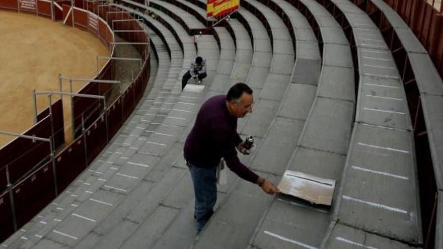 Un hombre pinta las rayas de los asientos de la plaza.