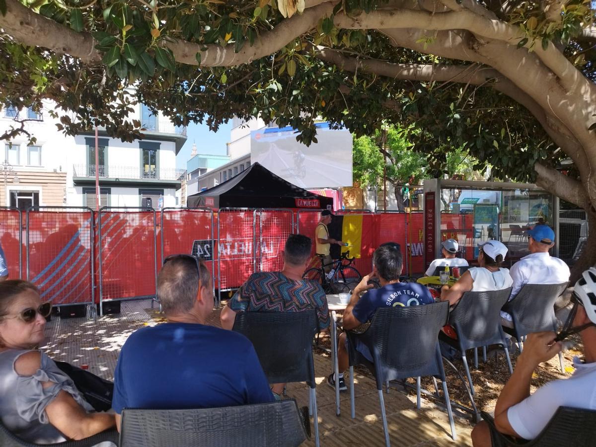 Aficionados se sientan bajo la copa de un árbol para ver la etapa de la Vuelta a España en Sevilla en una pantalla gigante