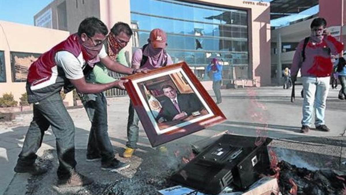 Tres estudiantes queman un retrato de Aguirre tras asaltar la sede del Gobierno estatal de Guerrero, este martes.