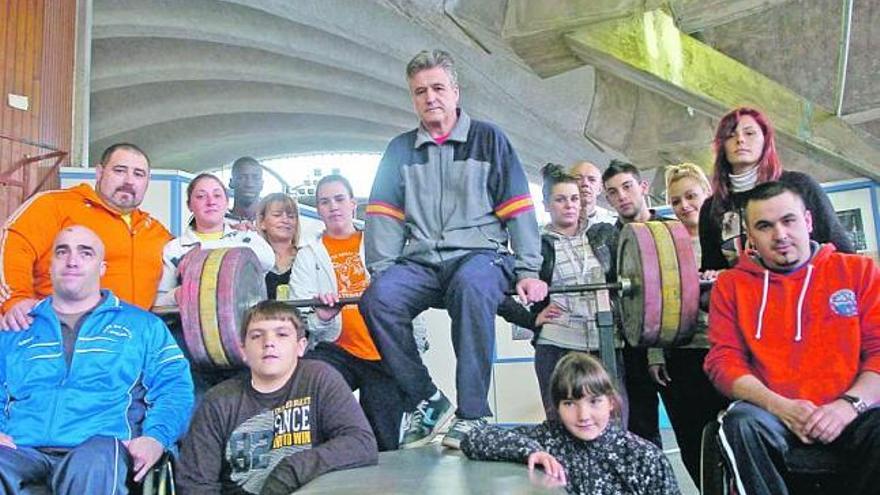 Lodario Ramón, en el centro, sentado en la barra, con algunos de los levantadores a los que entrena en el Palacio de los Deportes de Oviedo. / luisma murias