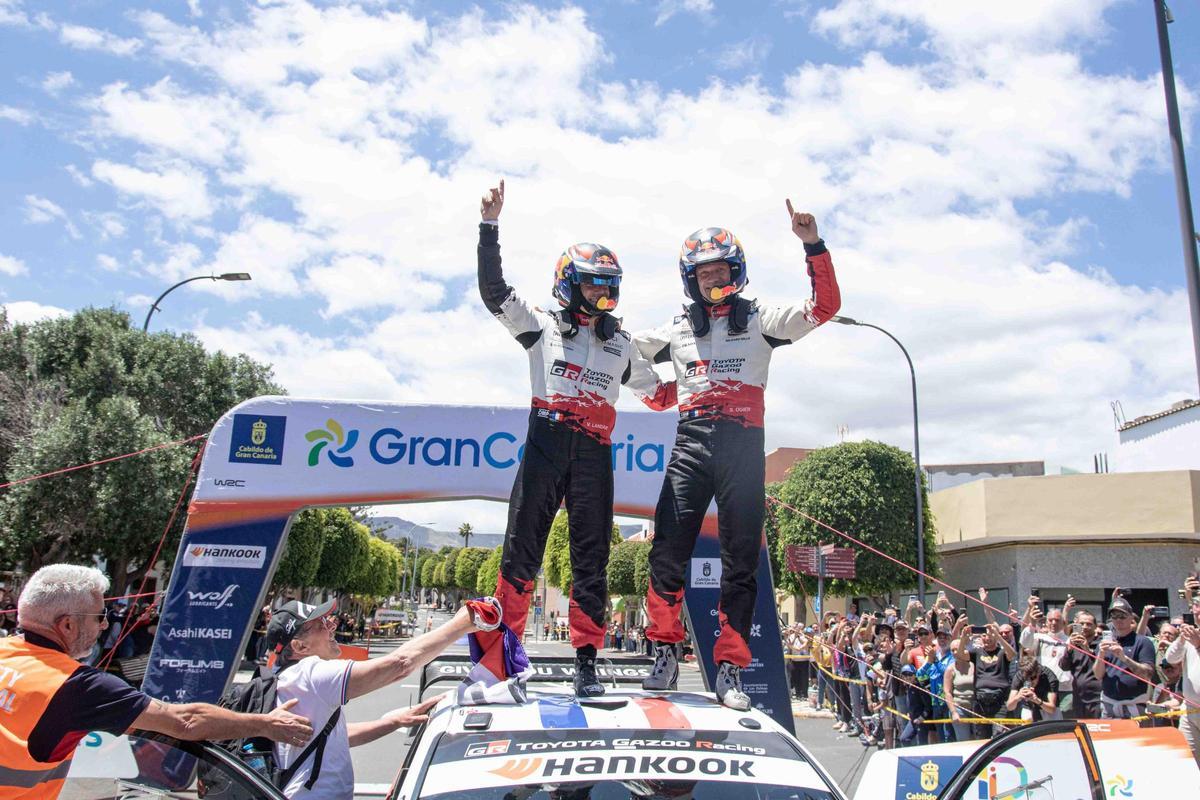Vincent Landais y Sébastien Ogier alzan sus dedos índices al cielo tras llegar a la meta del Rally Islas Canarias como ganadores.