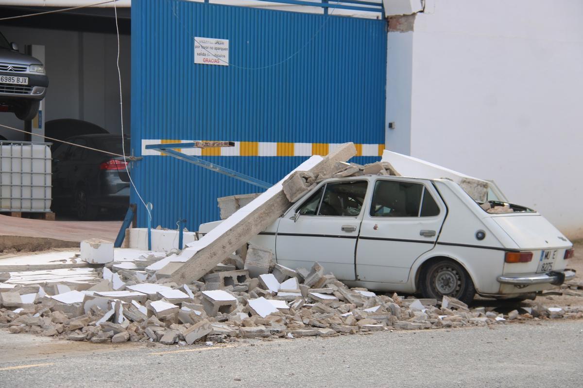El muro del taller mecánico ha impactado sobre un vehículo estacionado en la calle