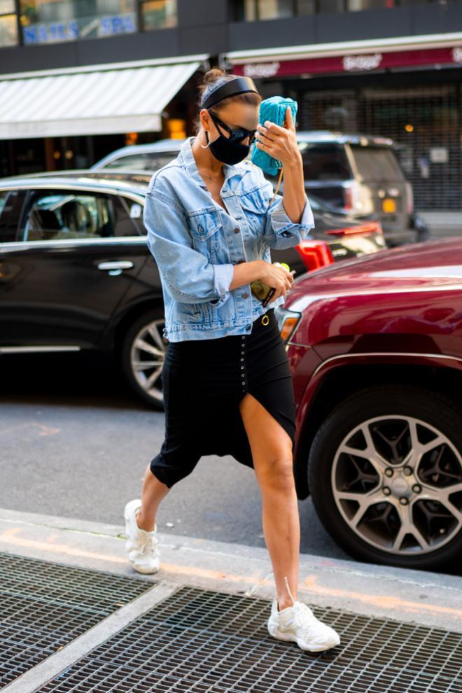 De look de Irina Shayk con chaqueta vaquera, falda midi y zapatillas de running blancas nos quedamos con su moño de bailarina con diadema