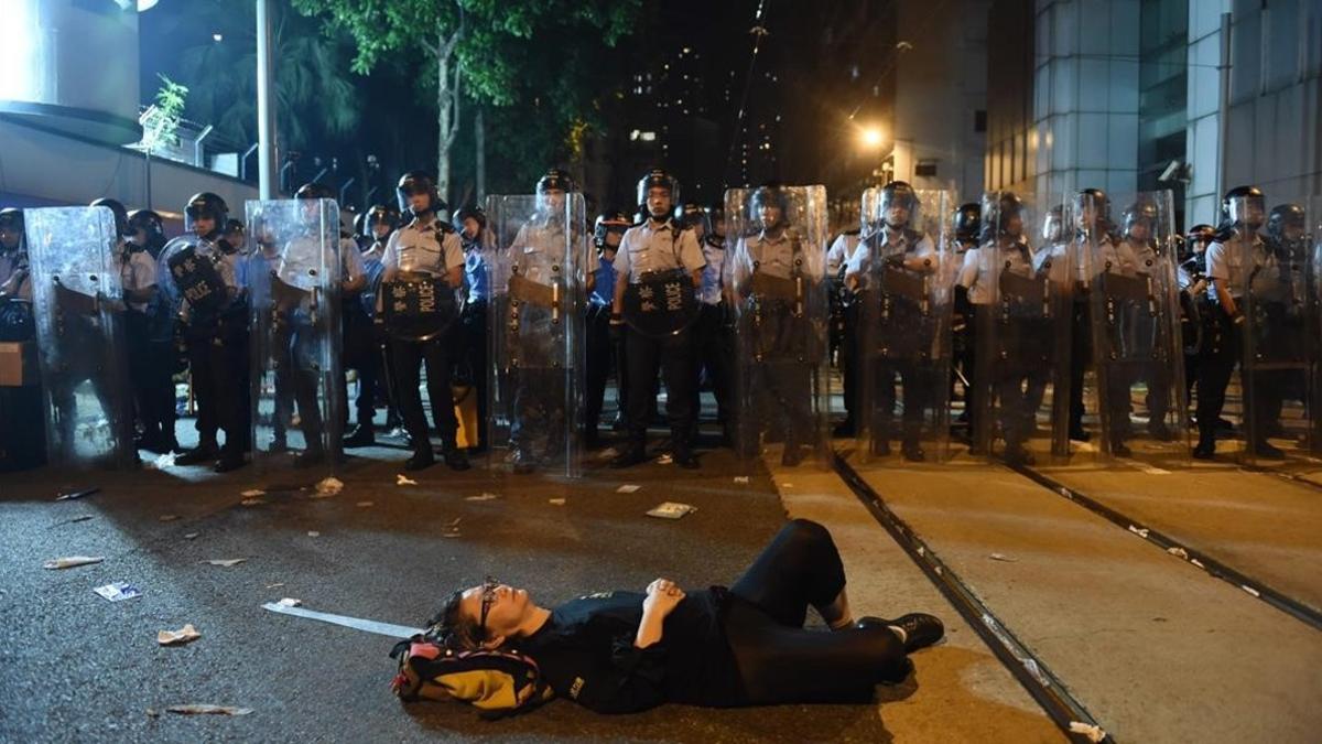 Una manifestante estirada en el suelo bloque una de las calles de Hong Kong frente a una fila de policías.