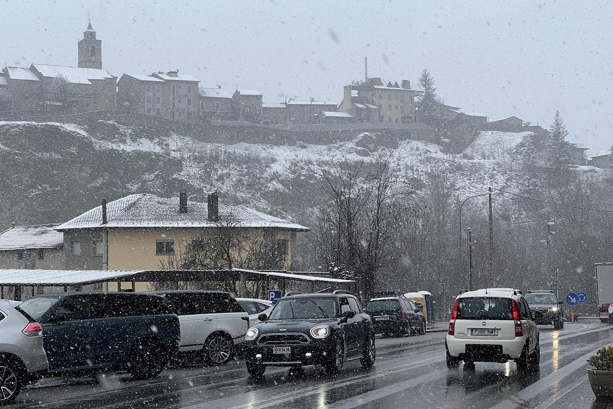 Vehículos circulando por la N-260, con el pueblo de Bellver de Cerdanya, nevado, al fondo.