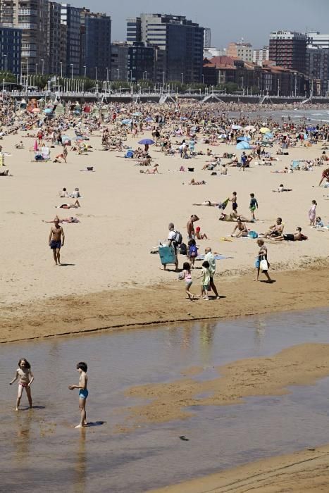 Gijoneses y visitantes se lanzan a la playa en una jornada calurosa.