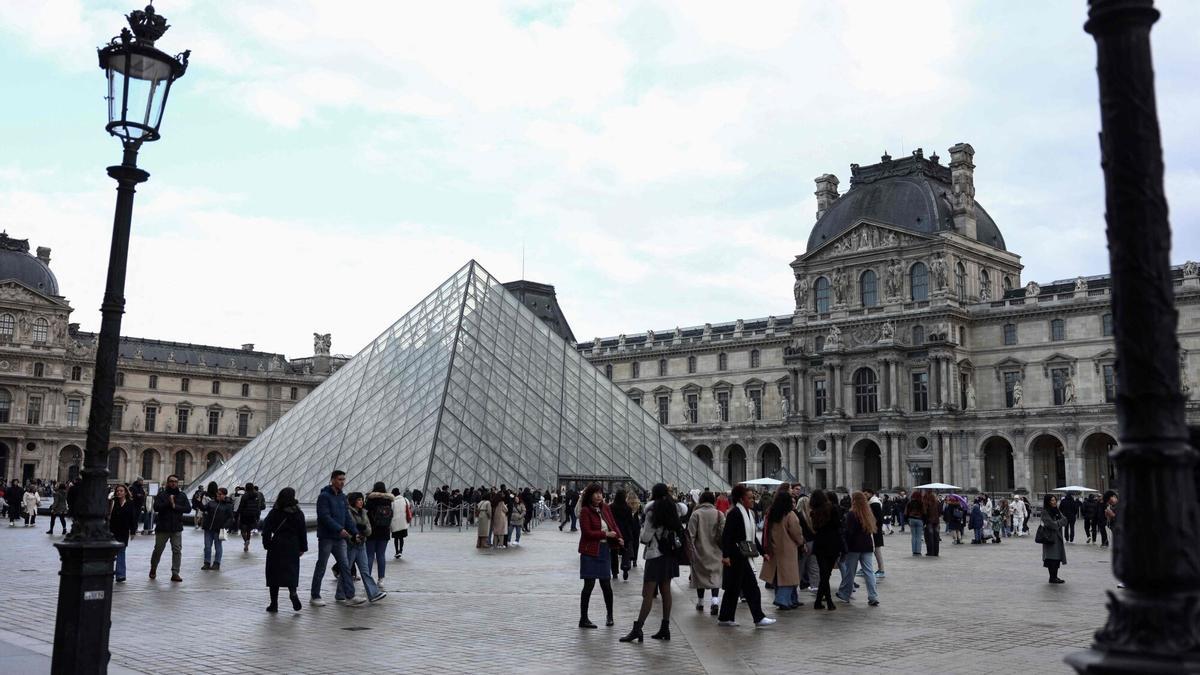 Turistas en el exterior del Museo del Louvre, con su icónica pirámide de cristal.