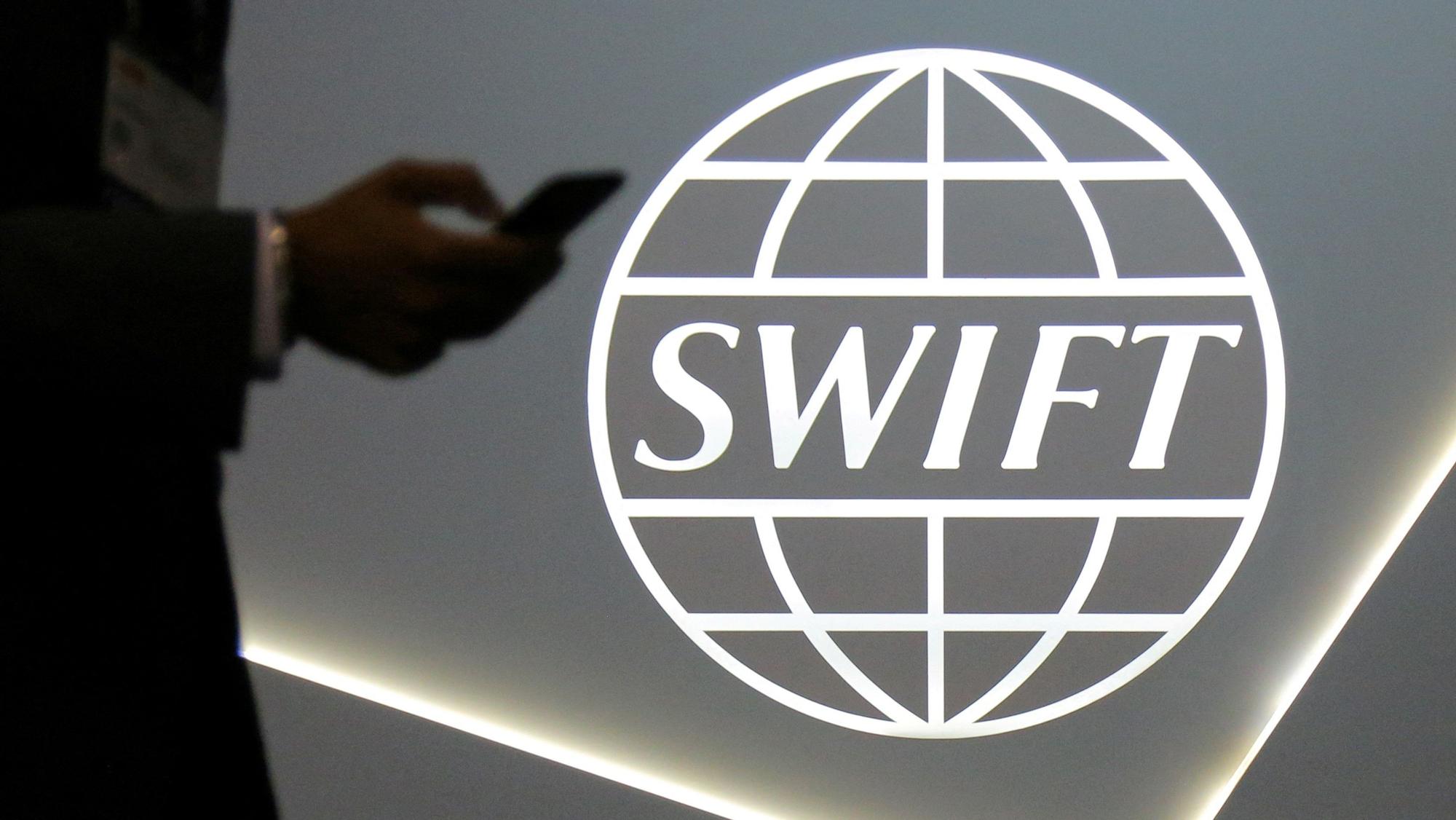 FILE PHOTO: A man using a mobile phone passes the logo of global secure financial messaging services cooperative SWIFT at the SIBOS banking and financial conference in Toronto, Ontario, Canada October 19, 2017. REUTERS/Chris Helgren/File Photo  NARCH/NARCH30