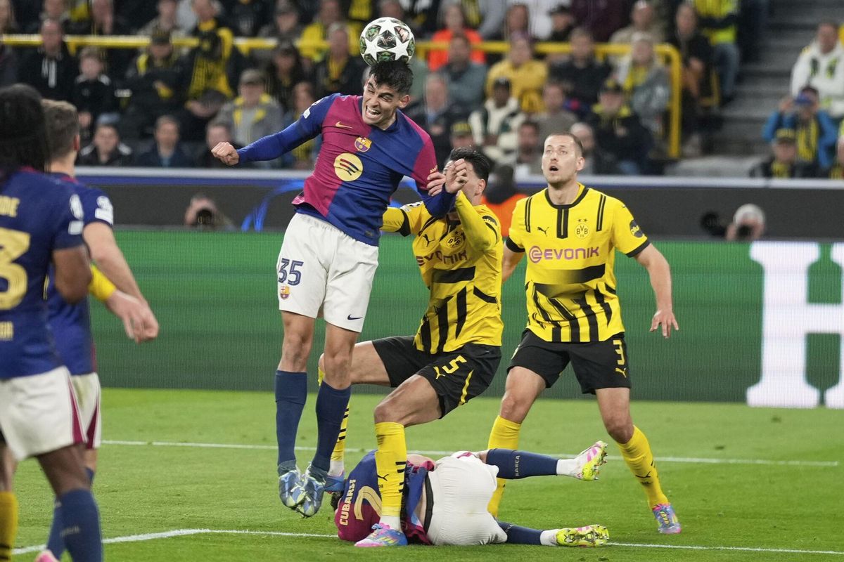 Barcelonas Gerard Martin, top, clears the ball past Dortmunds Ramy Bensebaini (5) during the Champions League quarterfinals second leg soccer match between Borussia Dortmund and Barcelona, at the Signa-Iduna Park in Dortmund, Germany, Tuesday, April 15, 2025. (AP Photo/Matthias Schrader)