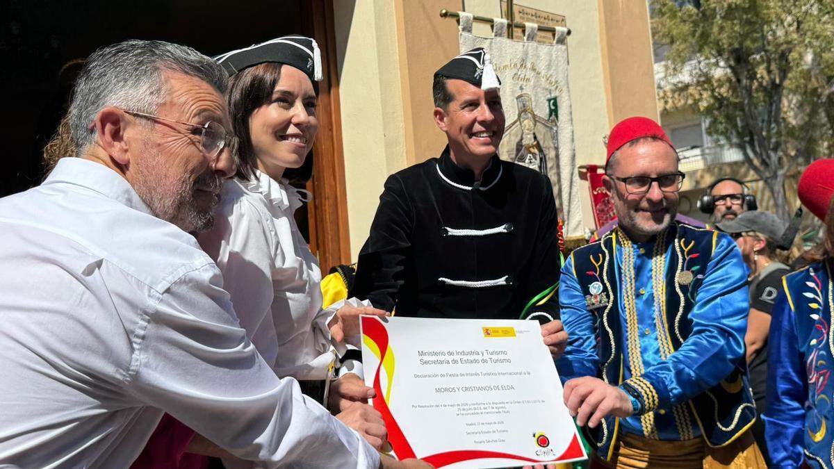 El subdelegado del Gobierno en Alicante, Manuel Pineda, la ministra Diana Morant, el alcalde de Elda, Rubén Alfaro, y el presidente de la Junta de Comparsas, Pedro Serrano, sujetan el diploma de la declaración de Fiestas de Interés Turístico Internacional.
