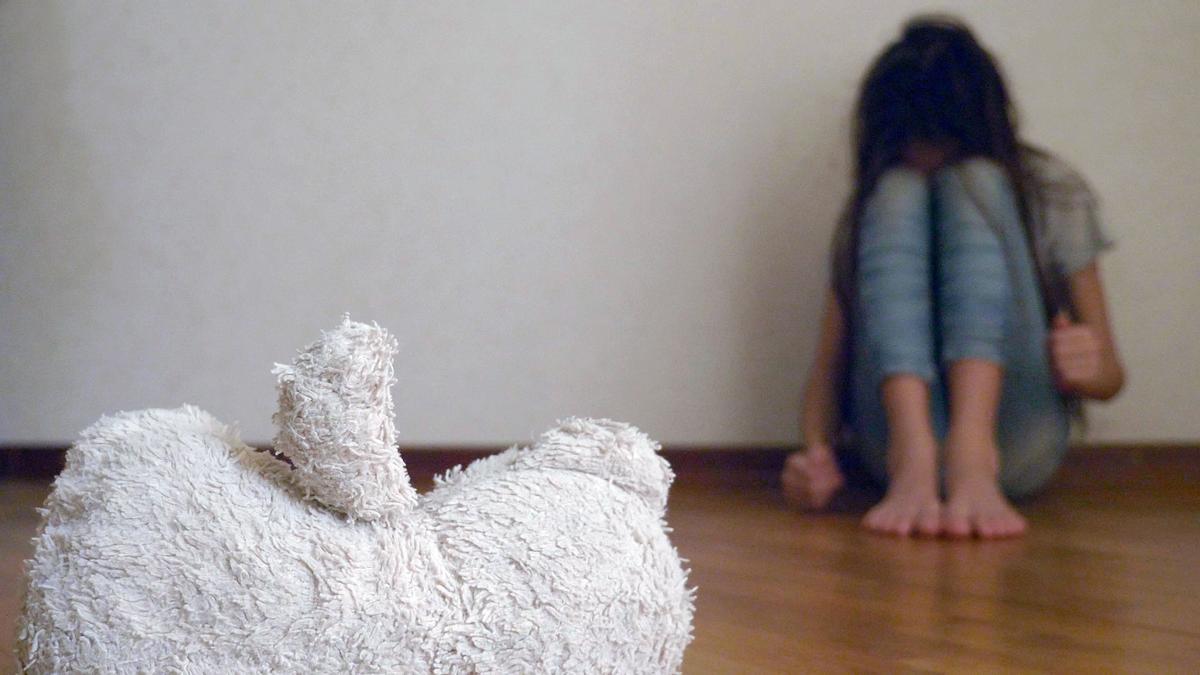 a desperate child in depression sits at the wall of his room, tries to attempt suicide. next to it is an abandoned soft toy. maltrato infantil