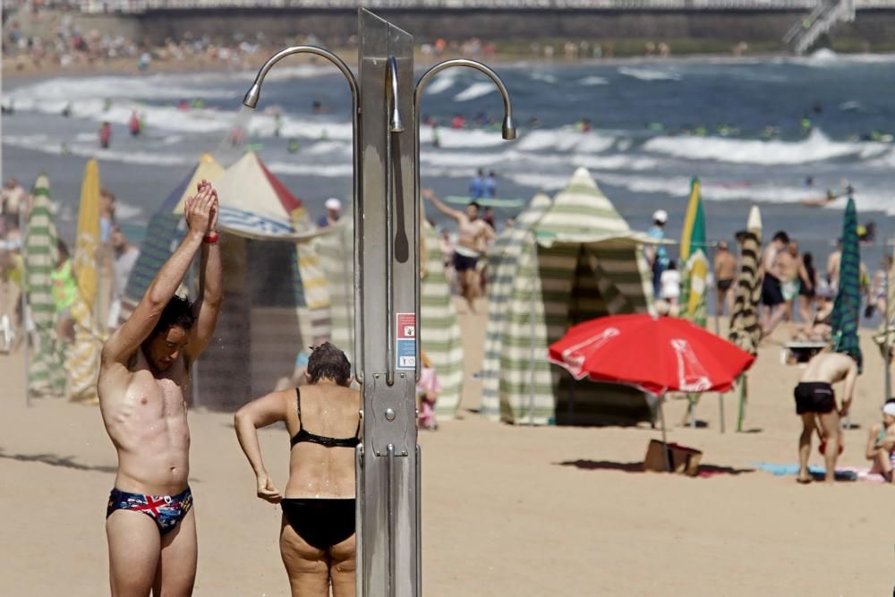 Gijoneses y visitantes se lanzan a la playa en una jornada calurosa.