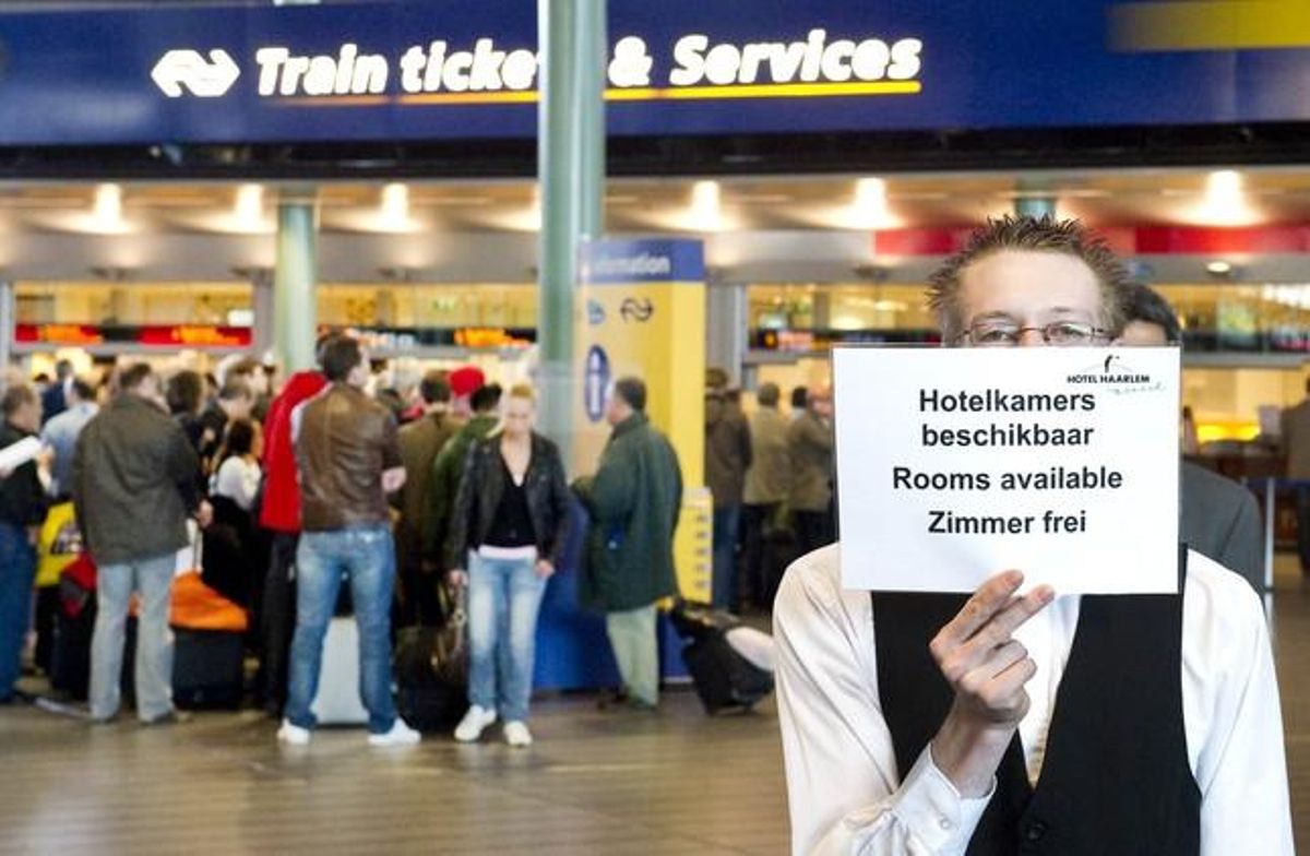 An employee of a hotel holds up a sign informing passengers of room vacancy as they stand in line to purchase train tiquets, at Schiphol Airport in Amsterdam