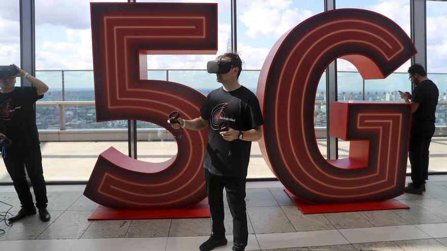 Un hombre juega con una consola de realidad virtual tras un logo del 5G