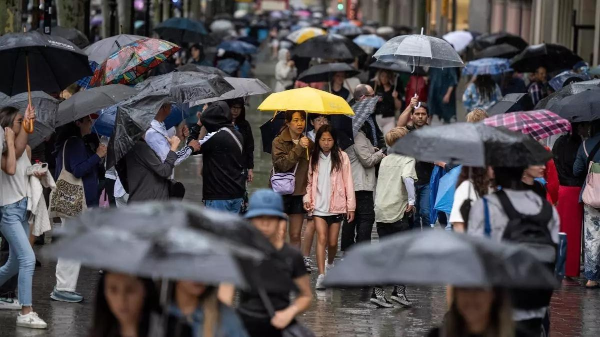 Personas se protegen de la lluvia. La Aemet prevé menos precipitaciones