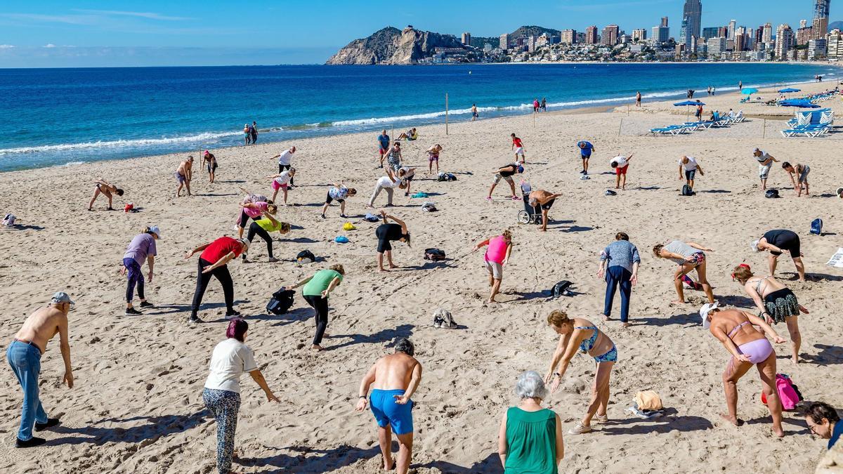 Jubilados practican gimnasia en la playa de Benidorm.