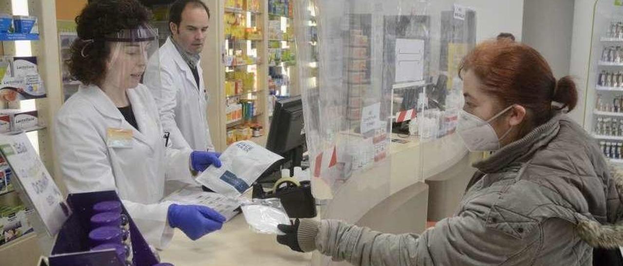 Una farmacéutica muestra una mascarilla a una clienta en la farmacia Negreira del Río de A Parda. // R.V.