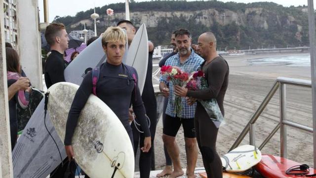 1. Al fondo, en el centro del pasillo formado por los surfistas, Ramón Rodríguez, padre de Jacobo, y, en primer término, Tiago, su hijo. 2. Tiago Rodríguez, con su tabla de surf, minutos antes de bajar a la arena de la playa de Salinas. 3. Los surfistas  amigos de Jacobo, camino a la orilla de Salinas.  4. Los familiares y amigos de Jacobo, entrando al agua con sus tablas. | |  BENJAMÍN LEBRATO / CHRISTIAN GARCÍA