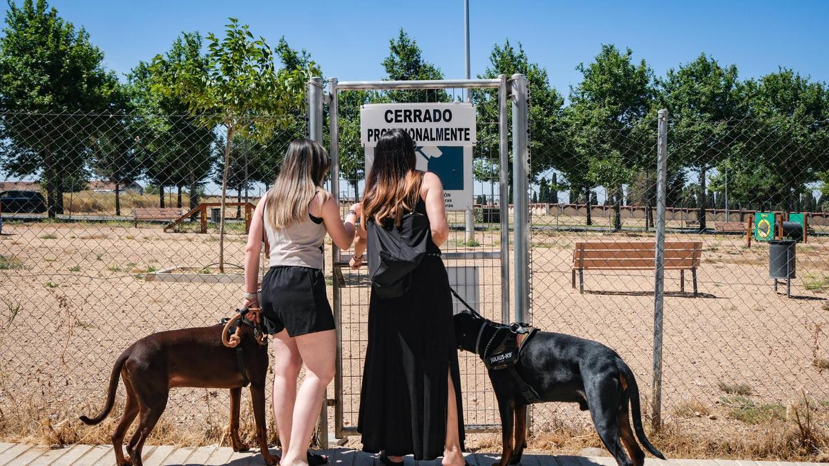Dos perros con sus dueñas, delante de la puerta cerrada del parque canino del Cerro del Viento, en Badajoz.