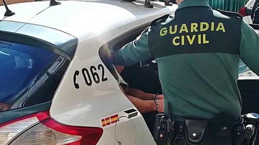 Un agente ayuda a entrar en el coche patrulla a uno de los detenidos.