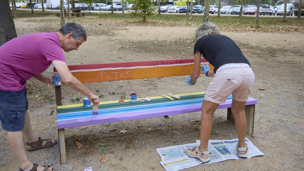 Dues persones pintant el banc vandalitzat del parc.