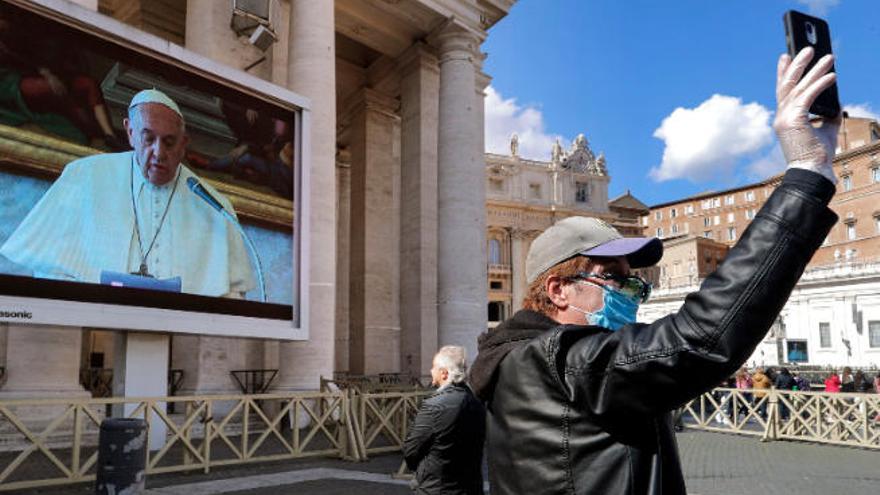 Un señor sigue la comparecencia del pontífice a través de una pantalla gigante, mientras otro se realiza un selfi.