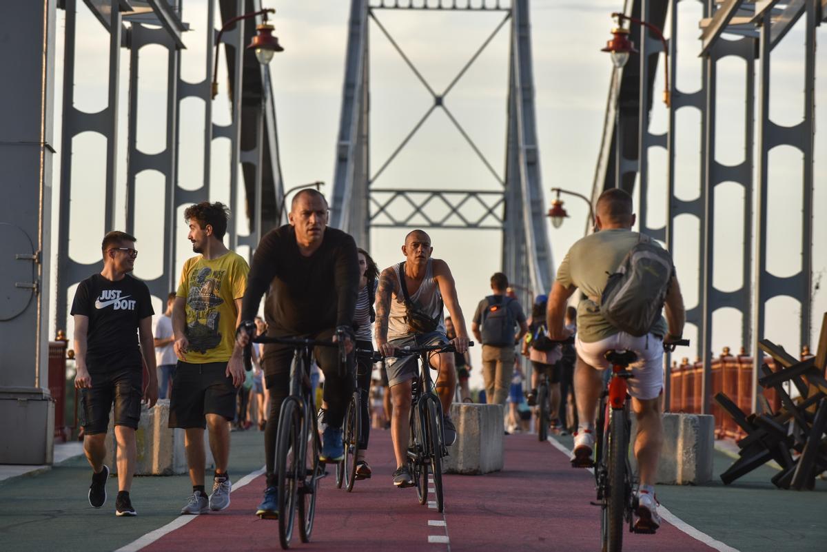 La gente cruza en bicicleta un puente peatonal sobre el río Dnipro