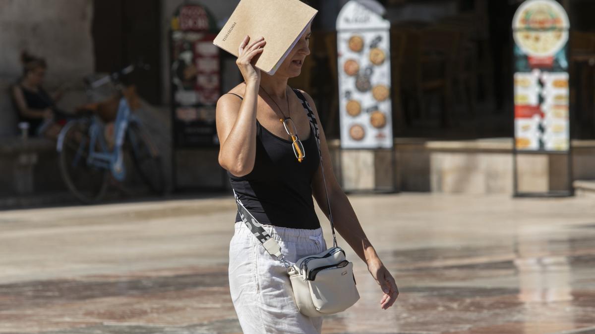 Una mujer pasea por el centro de València cubriéndose del calor.
