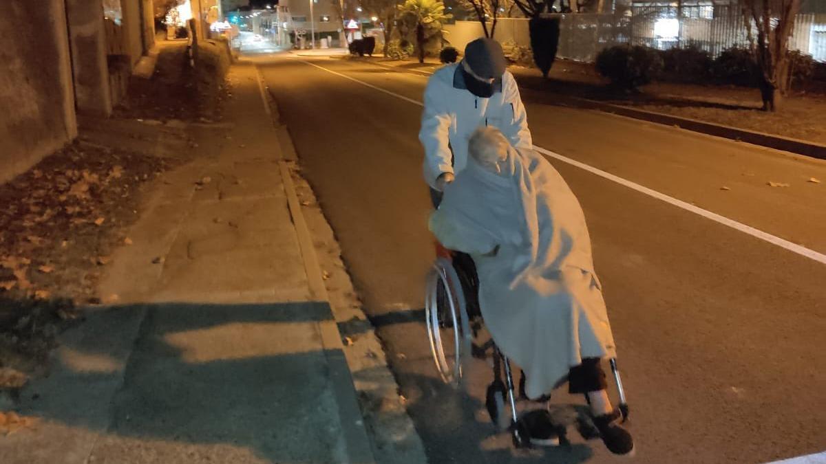 Un señor de 94 años empujando la silla de ruedas de su mujer con alzhéimer.