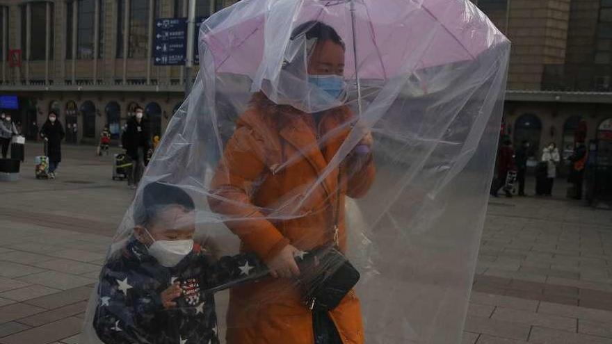 Una madre y su hijo se protegen con mascarillas y un plástico en una estación de tren de China. // EFE