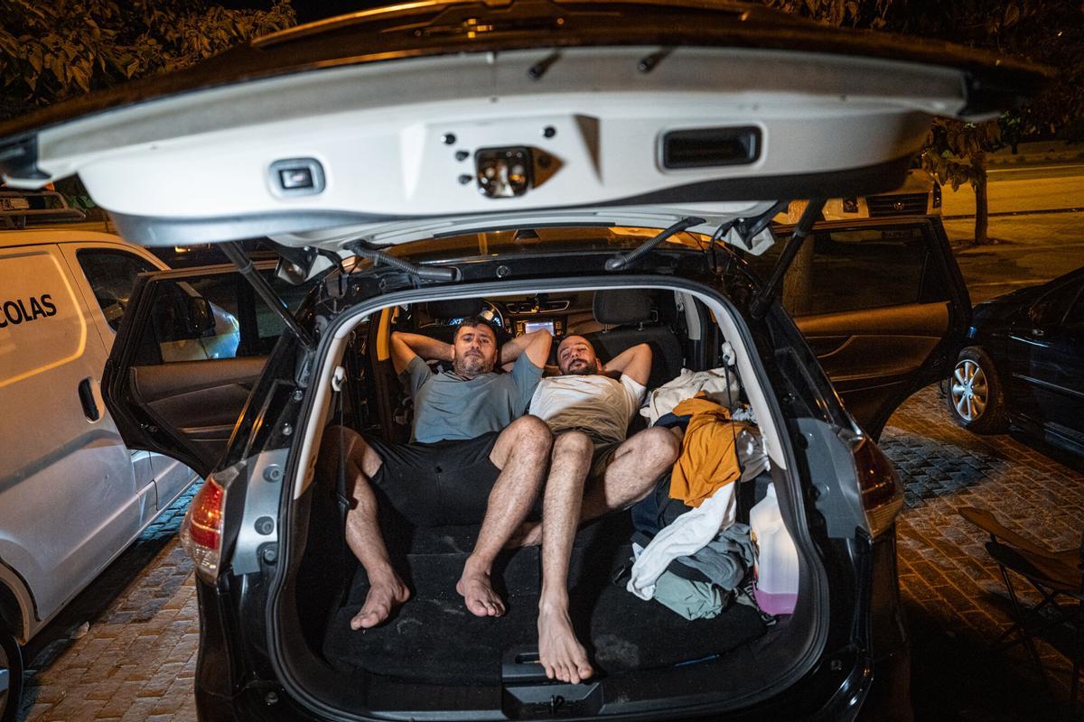 Mahmud y Mohamed, ambos de origen sirio, durante la entrevista. Uno reside en Países Bajos y el otro en Suiza. Han viajado en coche hasta Barcelona para pasar unos días de vacaciones, pero al encontrarse los alojamientos completos han decidido pasar la noche dentro del vehículo, estacionado frente al Port Olímpic. A 6 de agosto de 2026. Sociedad. AUTOR: MANU MITRU