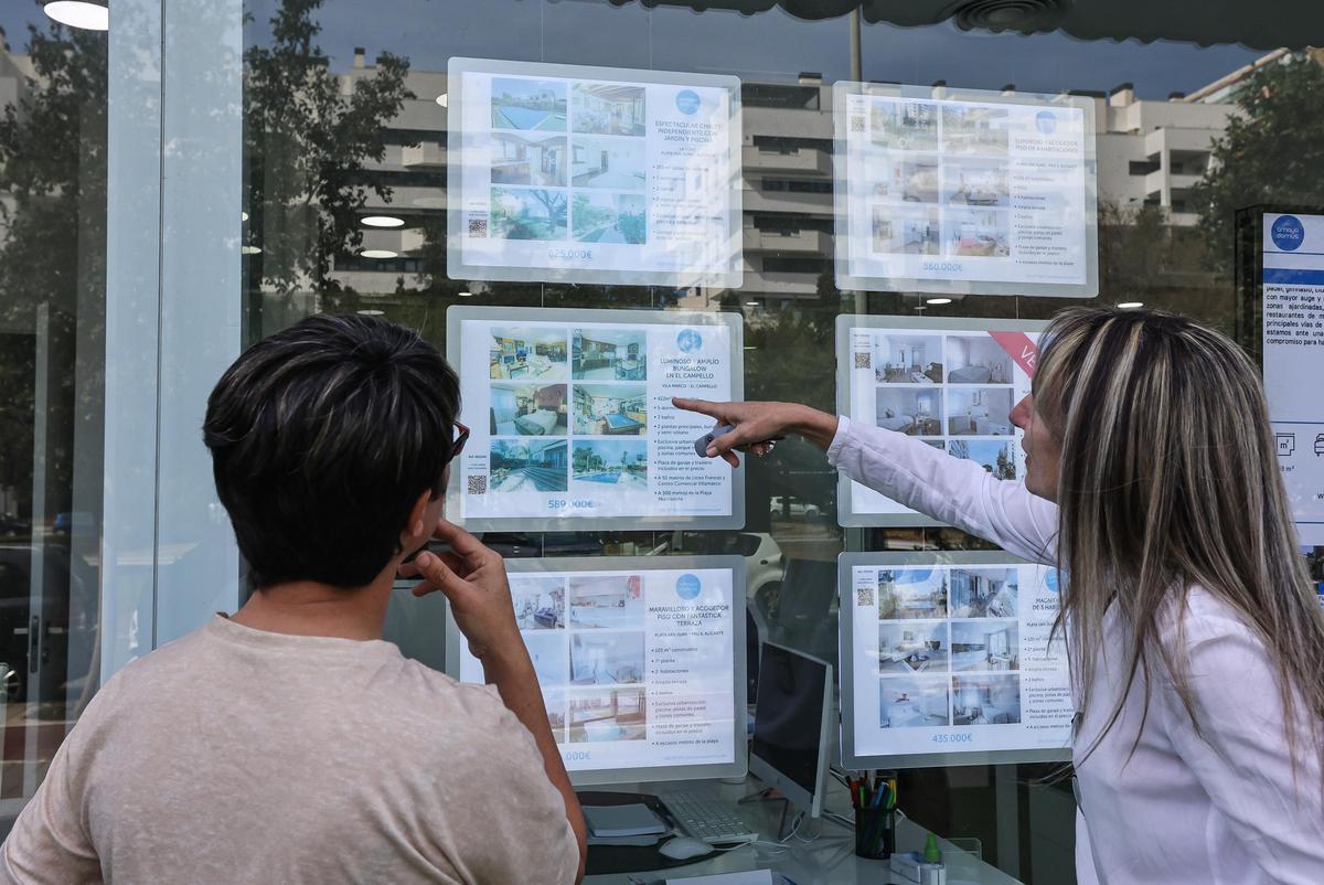 Dos jóvenes miran los anuncios de una inmobiliaria en Alicante.