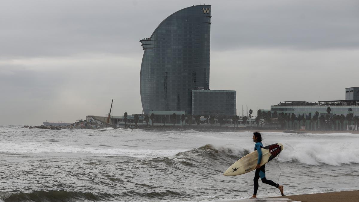 Un surfista se dispone a entrar en el agua de la playa de la Barceloneta con mal tiempo
