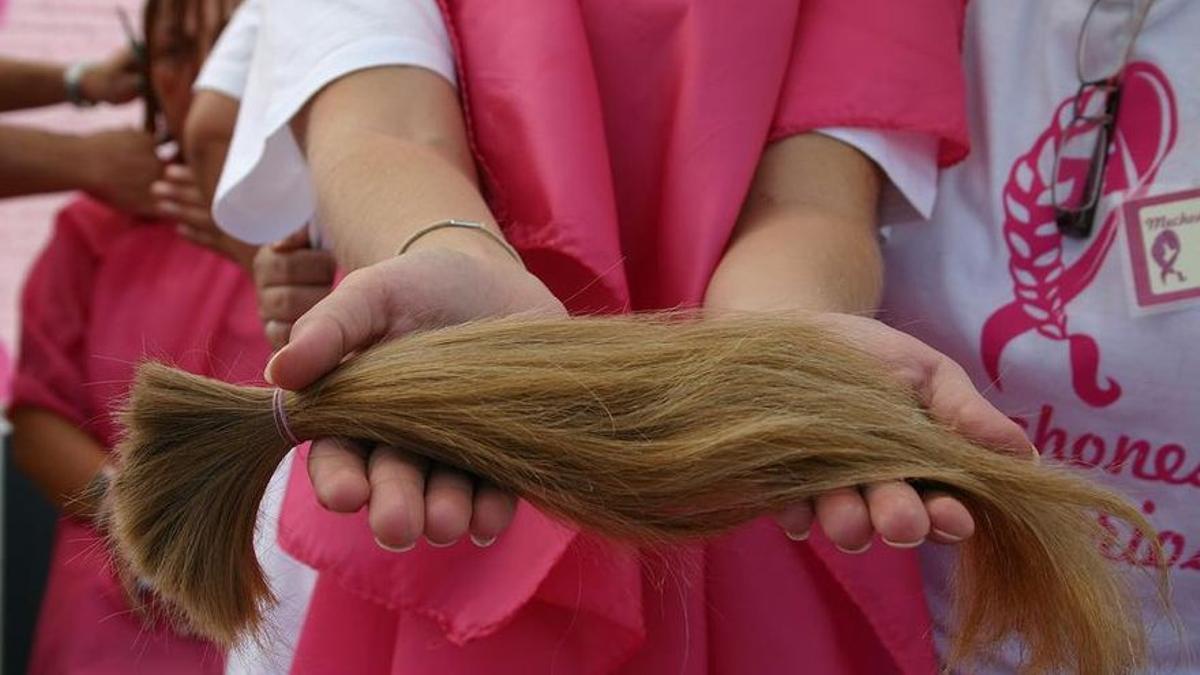 Una voluntaria muestra una coleta recién cortada para hacer una peluca solidaria.
