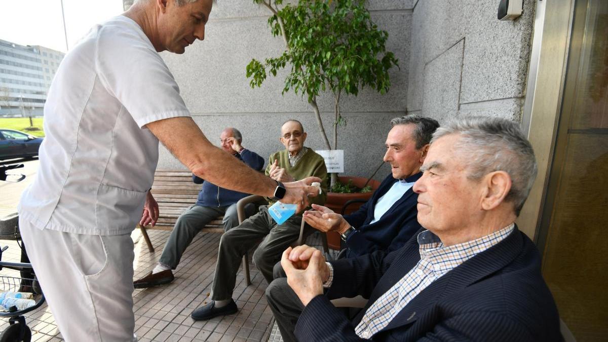 Un trabajador de una residencia de Pontevedra ofrece gel hidroalcohólico a varios usuarios. // G. Santos