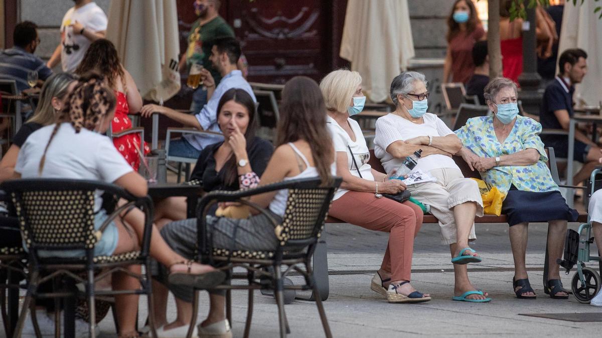 Personas mayores en un banco y jóvenes en una terraza, en la plaza Pedro Zerolo de Madrid, en agosto de 2020.