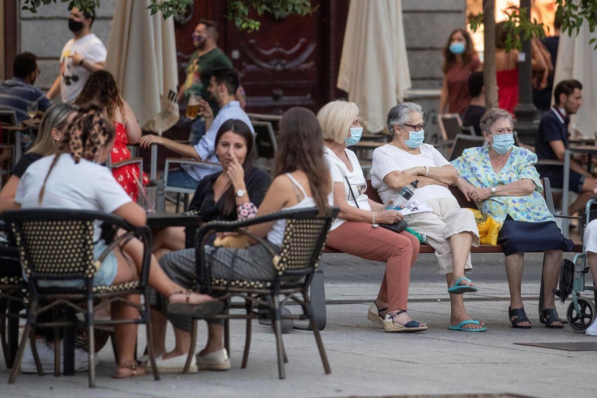 Personas mayores en un banco y jóvenes en una terraza, en la plaza Pedro Zerolo de Madrid, en agosto de 2020.