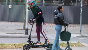 Un usuario de patinete, con un casco de moto, circula por una calle de Barcelona