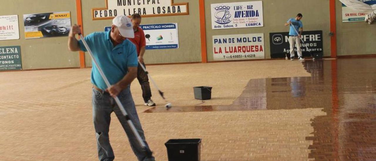 Tres operarios, durante las labores de barnizado de la cancha del polideportivo.