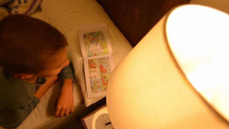 Un niño lee en su cama a la luz de una lámpara. // Gustavo Santos