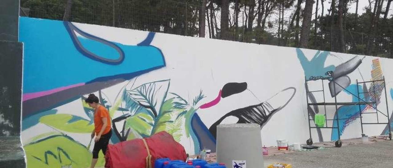 Paula Fraile dibuja el gigantesco mural en una pared de los campamentos de A Lanzada. // Faro
