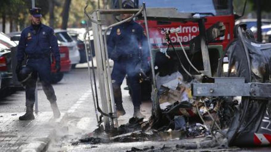 Varios agentes del Cuerpo Nacional de Policia observan un contenedor quemado en la calle Joan Reglá de Valencia durante la jornada de huelga general.