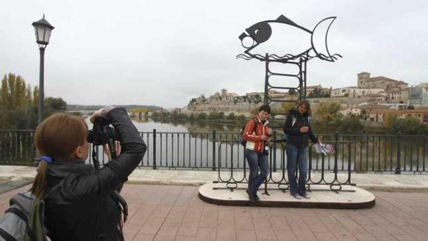 Unas turistas hacen una fotografía en la estatua de forja ubicada en el Puente de Hierro.