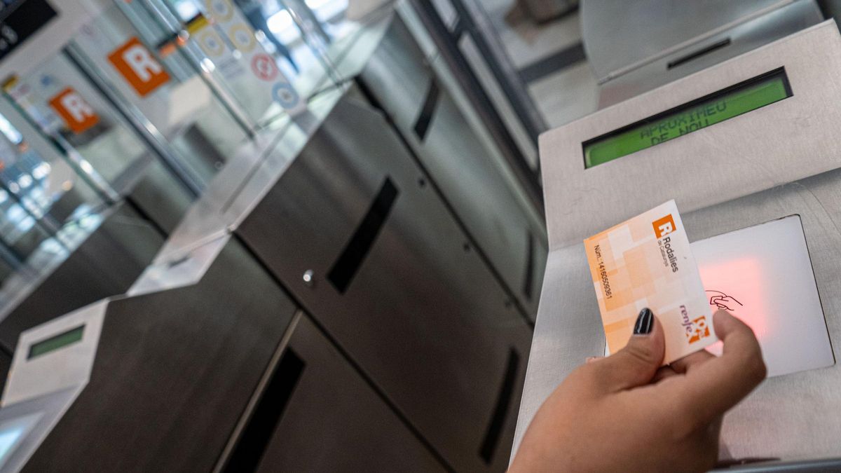 Una persona pasando el billete de Rodalies por la validadora de una estación de tren.