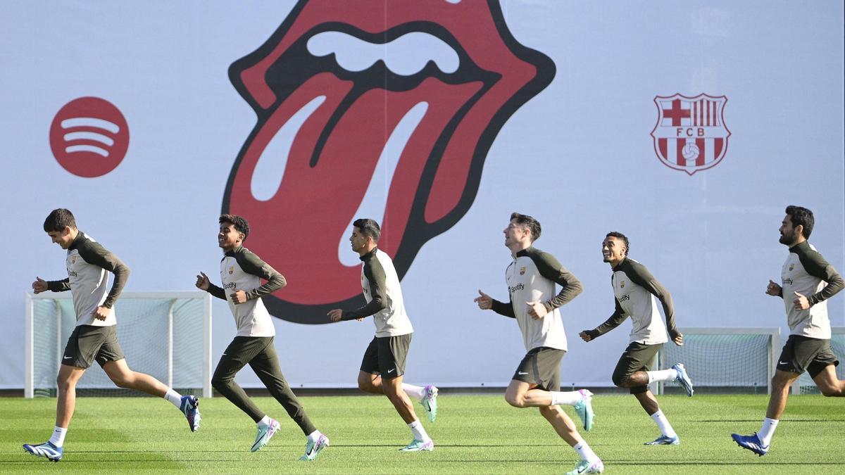 Varios jugadores del Barça corren delante del logotipo de los Rolling Stones en la ciudad deportiva.